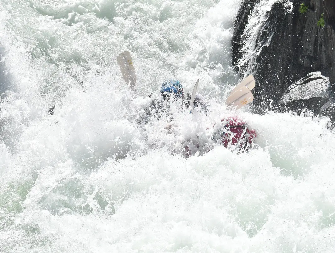 Rafting through whitewater rapids while paddling in sync.